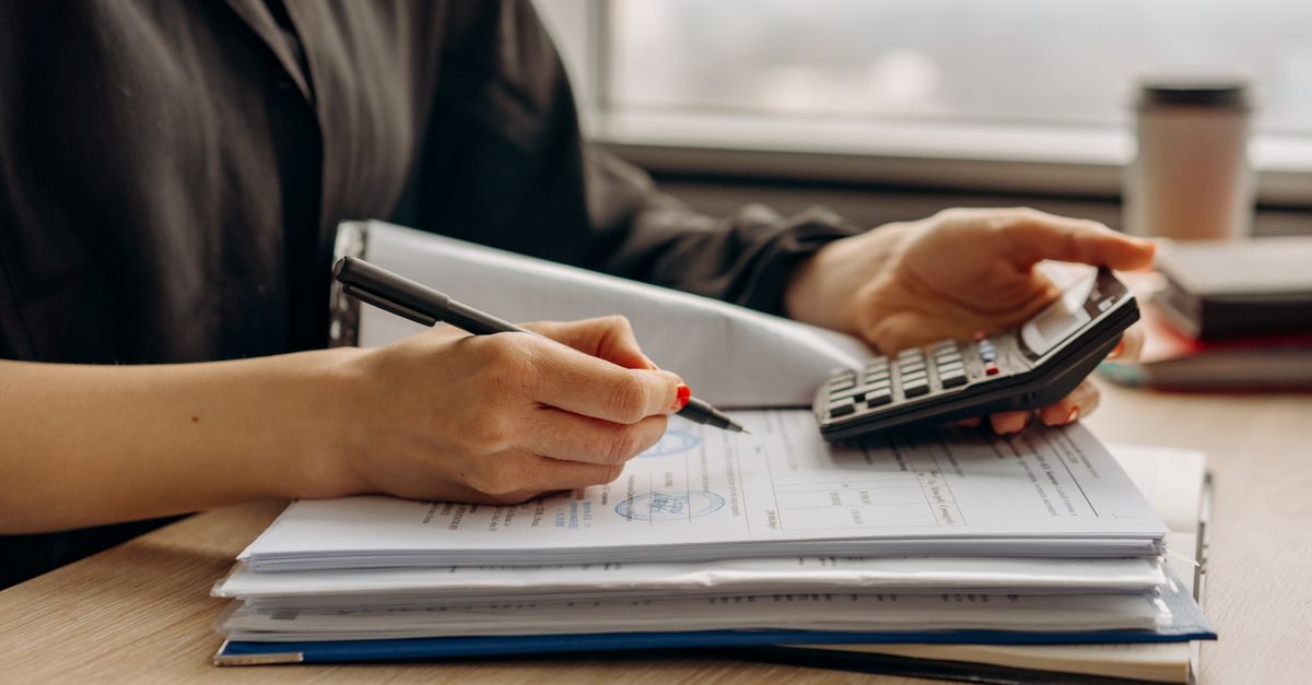 Persona haciendo cálculos con una calculadora sobre documentos financieros en una oficina.