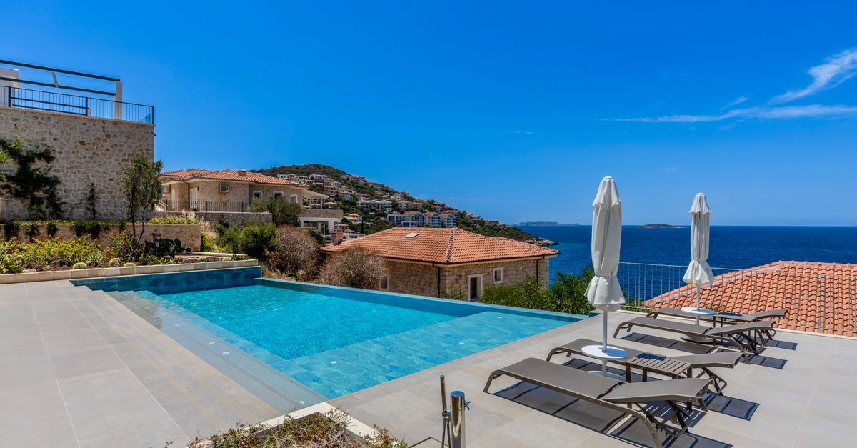 Villa mediterránea con piscina infinita y vistas al mar bajo cielo despejado.