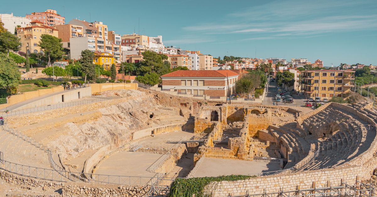 Anfiteatro romano de Tarragona junto al mar, con la ciudad al fondo bajo un cielo despejado.