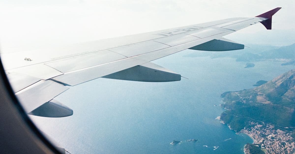 Ala de avión vista desde la ventanilla sobre una costa mediterránea con una población junto al mar.