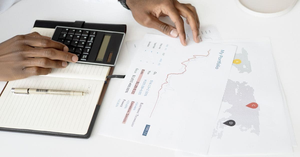 Hands working a calculator beside an investment report with a world map