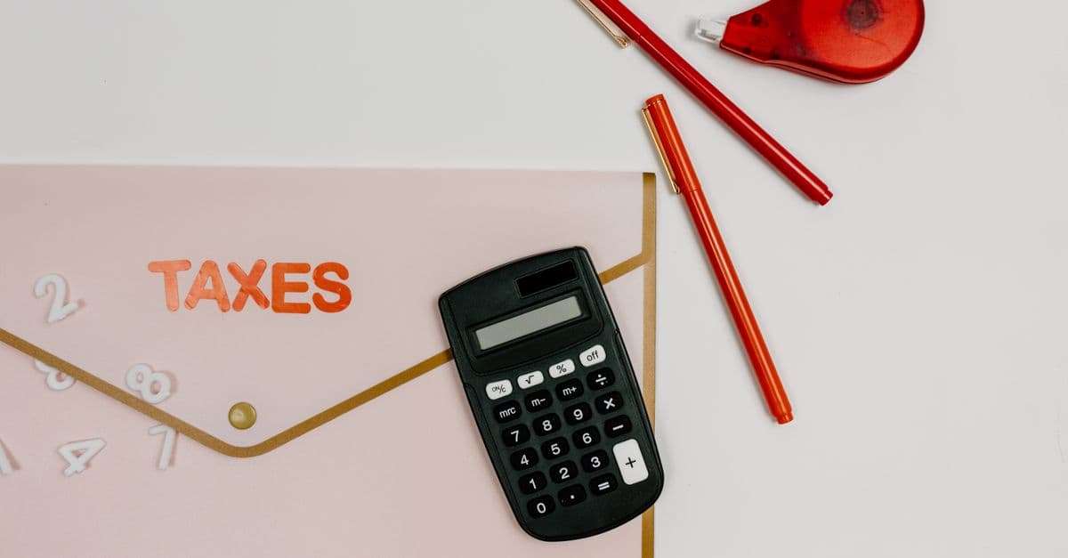 Calculator and red pens on a pink folder labelled Taxes
