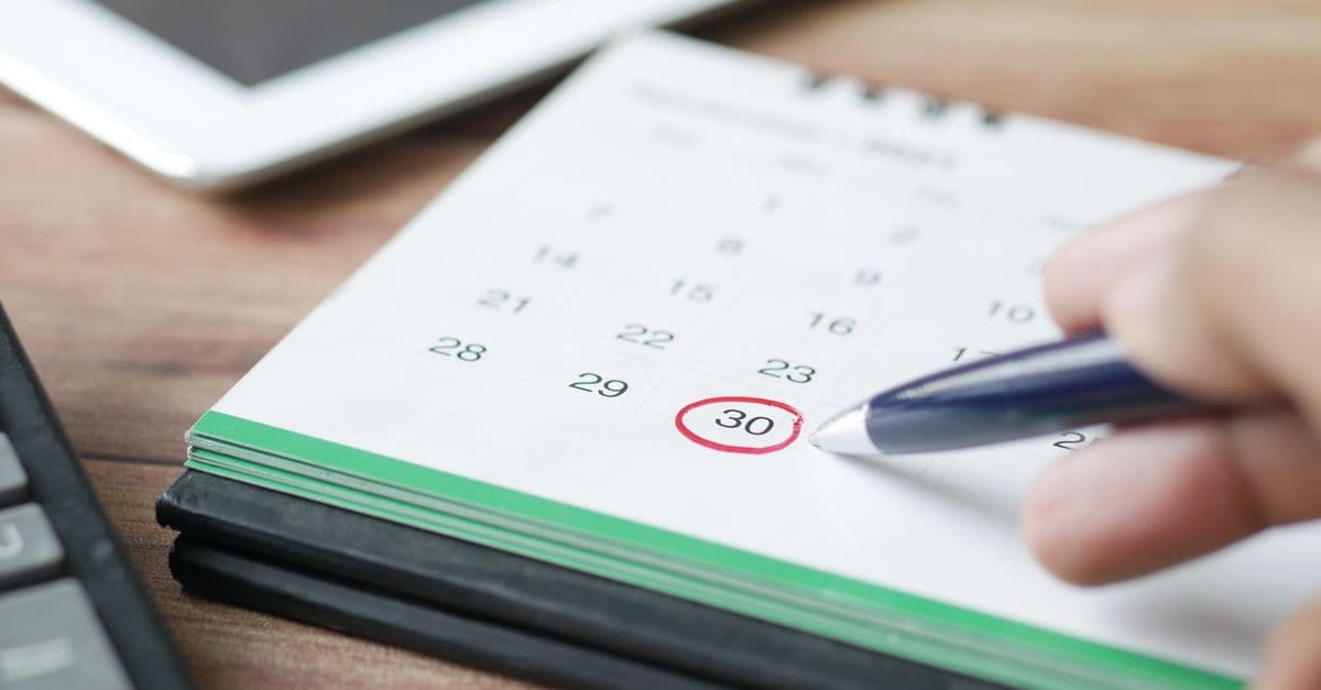 Hand circling a date on a desk calendar with a pen